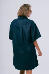 Vestido corto de denim azul oscuro, con cuello camisero, mangas cortas, cierre frontal con botones, bolsillo aplicado en el pecho y calce holgado.