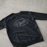 Buzo de cuello redondo Eseele Club Stone con acabado stonewash en color negro lavado, corte oversize y diseño relajado. Presenta logo ovalado retro en la espalda y terminaciones acanaladas.