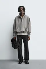 Sudadera de corte boxy fit en color gris, confeccionada en tejido de algodón con interior afelpado. Presenta cuello solapa, cierre frontal con botones a presión, manga larga con puños acanalados y bolsillo frontal tipo canguro. El bajo cuenta con un acabado elástico.