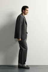 Blazer de corte regular fit color gris oscuro, confeccionado en tejido con lana. Cuenta con cuello con solapas de muesca, cierre frontal con tres botones, bolsillos con solapa en la cadera y un bolsillo de vivo en el pecho.