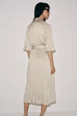 Vestido midi de Zara Woman Collection color beige, con cuello solapa, mangas por debajo del codo y diseño cruzado. Confeccionado en tejido plisado con brillo satinado, incluye un cinturón ajustable del mismo género con lazada en la cintura.