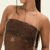 Collar tipo choker y tiras colgantes, compuesto por pequeñas cuentas plateadas. El diseño incluye un choker ajustado al cuello y dos tiras largas que caen sobre el pecho y los hombros, sujetas a una prenda negra con un broche metálico central.