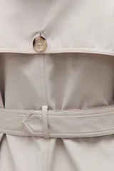 Trench impermeable color beige de corte clásico, con cierre frontal de doble botonadura, solapas amplias y cinturón ajustable con hebilla. Incluye capucha desmontable y bolsillos laterales.