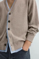 Cárdigan de punto con cuello en pico y manga larga. Presenta un diseño de ajuste relajado con cierre frontal de botones y acabados en rib con efecto doble en color azul a contraste sobre la base color topo.