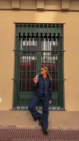 Camisa de jean azul oscuro con cuello redondo, cierre frontal de botones y mangas abullonadas con puños ajustados.