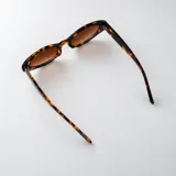 Lentes de sol con armazón carey de diseño ovalado, patillas anchas con detalle de pespuntes metálicos y cristales marrones degradados.