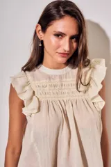 Blusa sin mangas de color crudo, con diseño oversize, cuello redondo y detalles de nido de abeja bordado en el pecho, acompañado de volados en los hombros.