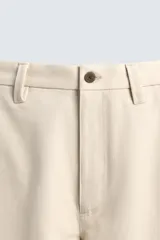 Pantalón chino de corte relajado, confeccionado en tejido estructurado de color beige. Presenta bolsillos frontales, bolsillos traseros de vivo y cierre frontal con cremallera y botón.