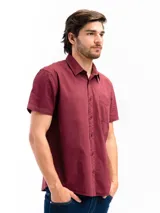 Camisa de manga corta color celeste claro, confeccionada en algodón, con cuello clásico y un bolsillo de parche en el lado izquierdo del pecho.