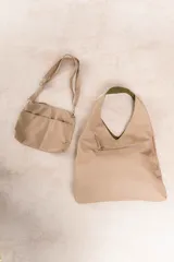 Bolso de hombro color beige, confeccionado en cuero sintético con interior plateado. Presenta un bolsillo externo con cierre.