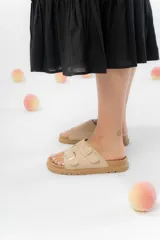 Sandalias color beige con dos tiras anchas con hebillas metálicas doradas, confeccionadas en material gamuzado sintético. Suela acolchada y antideslizante.