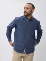 Camisa de manga larga en algodón tramado, con cuello clásico abotonado y cierre frontal con botones. Presenta un diseño liso con textura visible y un pequeño bordado en la pechera.