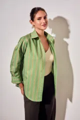 Camisa de corte oversize con estampado de rayas verticales en tonos verde, blanco y ocre. Presenta cuello clásico, cierre frontal con botones, bolsillo en el pecho y mangas largas con puños abotonados.