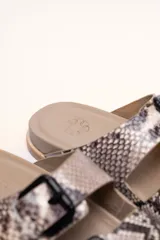 Sandalias de cuero color negro con dos tiras anchas sobre el empeine, cada una con hebillas metálicas ajustables y detalles de tachas plateadas. La suela es de cuero con un borde de color madera.