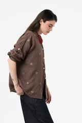 Camisa de lino color chocolate, de corte relajado y mangas largas con detalles bordados florales en contraste. Cuenta con cuello clásico y cierre frontal de botones.