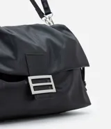 Cartera tipo shoulder bag de tamaño grande, confeccionada en poliuretano con acabado que imita el cuero. Presenta un diseño desestructurado con solapa superior, cierre mediante cordón de ajuste y detalles metálicos plateados en el frente. Incluye correa ajustable para llevar al hombro o cruzada.