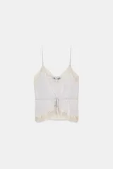 Top satinado color lila claro con escote en pico y tirantes finos. Presenta detalles de encaje color crema en el escote y el bajo, y una lazada ajustable en la cintura.