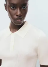 Jersey de punto fino color blanco crudo, con cuello polo, manga corta y diseño entallado con canalé.