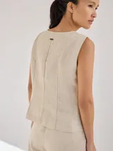 Chaleco sin mangas de lino, con diseño de paneles en color blanco crudo y beige. Presenta escote redondo y cierre frontal con botones de madera marrones.