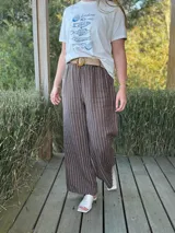 Pantalón de lino marrón con rayas verticales blancas, corte recto, cintura con elástico ancho y cinturón de rafia extraíble.