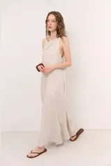 Vestido largo color beige, de corte amplio y sin mangas, con escote redondo y aberturas laterales pronunciadas en las sisas.