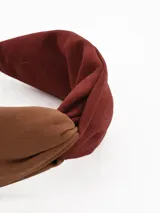 Vincha de tela con diseño de nudo central, combinando tonos marrón y bordó.