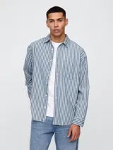 Camisa de jean de manga larga con estampado de rayas verticales en tonos azul y blanco. Presenta cuello clásico, cierre frontal con botones y un bolsillo en el pecho.