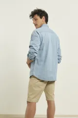 Camisa de hombre de denim azul, manga larga, con cuello buttondown y un bolsillo de parche en el pecho izquierdo.