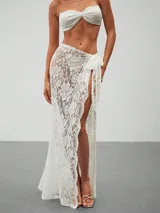 Pareo largo de encaje blanco con estampado floral, corte maxi y abertura lateral alta, anudado en la cintura con un lazo.