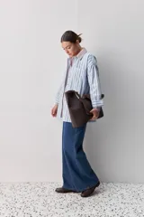 Camisa de calce relajado con diseño a rayas verticales en tonos azul y blanco, cuello clásico, mangas largas con puños abotonados y cierre frontal con botones. Presenta bolsillos aplicados en el delantero y una silueta versátil.