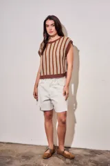 Chaleco de punto sin mangas con diseño de rayas verticales en tonos marrón, blanco y mostaza. Presenta cuello redondo y terminaciones acanaladas en color marrón sólido.