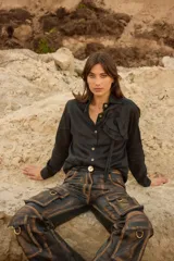 Camisa holgada blanca con detalle de roseta de tela en el frente, cuello camisero, botones a tono y diseño ligeramente más largo en la parte trasera.