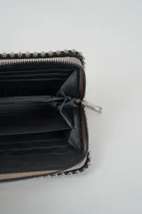 Billetera rectangular color celeste claro, con borde decorado con tachas metálicas plateadas y cierre de cremallera plateado en el lateral.