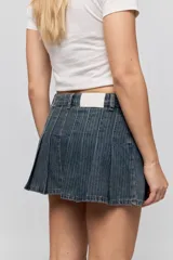 Minifalda de jean azul con diseño de tablas y patrón de rayas verticales finas. Presenta un corte corto y bolsillos laterales.