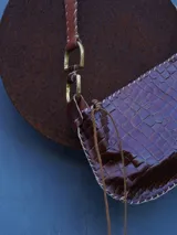 Cartera de cuero crocco con herrajes en bronce, silueta curva, terminación artesanal en los bordes y correa de hombro ajustable con detalles metálicos.