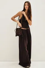 Pantalón de corte sastrero y pierna ancha, color marrón oscuro, con pinzas en la cintura y cierre frontal con lazo ajustable.