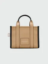 Cartera tipo tote bag Marc Jacobs en color tostado, con detalles en negro y blanco. Cuenta con las inscripciones "THE TOTE BAG" y "MARC JACOBS" estampadas en el frente. Posee doble asa de mano superior y correa de hombro ajustable y desmontable.