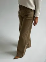 Jean de corte recto y tiro medio, en color camel con acabado desgastado. Presenta diseño clásico de cinco bolsillos, cierre frontal con botón y cremallera, y costuras reforzadas en el ruedo.