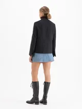 Chaqueta de paño gris con cuello mao y cuello desmontable con volados de gasa y puntilla. Presenta cierre frontal con botones metálicos, cuatro bolsillos delanteros con solapa y vivos en satén color chocolate que recorren el diseño.