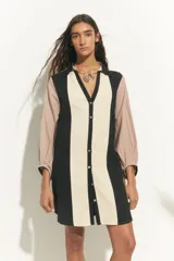 Túnica corta de algodón con cuello clásico y mangas largas. Presenta un diseño de bloques de color en negro, beige y rosa pálido.