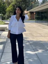 Camisa blanca de manga larga con cuello clásico y botones frontales. Presenta volantes escalonados en la parte delantera.