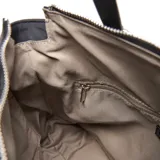Cartera tipo tote de tela técnica color negro, con doble asa de mano y correa de hombro ajustable. Presenta múltiples bolsillos frontales con cierre metálico, logo circular de la marca en el frente y detalle de cordón decorativo con argollas.