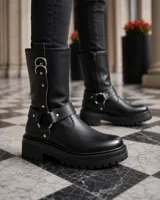 Botas de caña media en cuero negro, con suela track dentada y taco cuadrado. Presentan un diseño con correas ajustables, argollas metálicas y detalles de tachas plateadas.