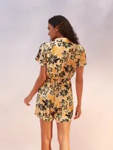 Mono corto negro con estampado floral en tonos beige y amarillo. Presenta cuello camisero, manga corta y un lazo ajustable en la cintura.