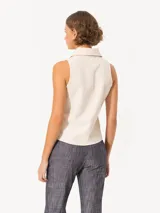 Camisa sin mangas confeccionada en tela de punto lisa, color crema, de corte regular. Lleva cartera con broches JCH y pinzas que entallan la prenda.