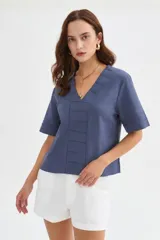 Blusa de viscosa color beige con cuello en V, mangas cortas amplias y detalles de pespuntes decorativos en el frente y las mangas.