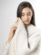 Ruana de punto color beige con sutiles motas multicolores, con bordes terminados en flecos largos.