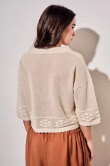 Cardigan de algodón peinado color beige, con cuello camisero, cierre frontal de botones y detalles de textura en crochet con diseño de flores. Mangas tres cuartos y diseño corto.