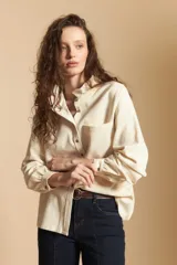 Camisa de pana color crema con cuello camisero con volados, cierre frontal de botones y mangas largas con puños abotonados. Presenta un bolsillo aplicado en el pecho y una silueta relajada.