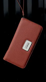 Billetera larga con cierre perimetral, confeccionada en material sintético texturizado color mostaza. Cuenta con correa de mano extraíble y placa metálica con logo de la marca en el frente.